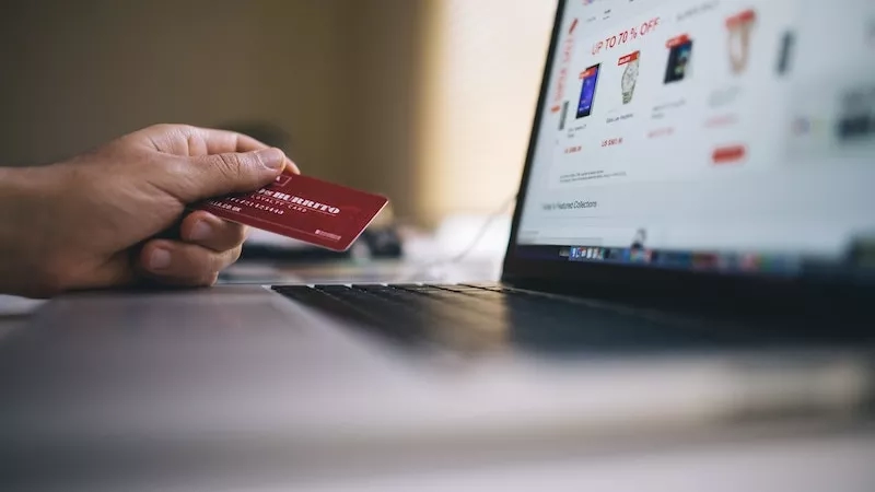 A person holding a red card in front of a laptop with an online shopping site open.