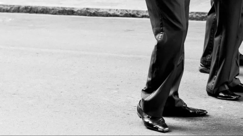 A black and white photo of a man wearing a suit standing on the side of the road.