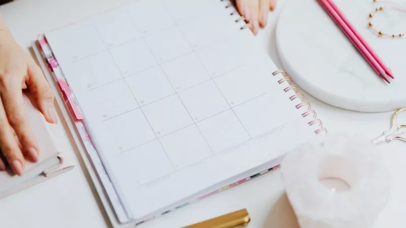 A woman is sitting at a desk with a calendar, pens, and other office supplies.