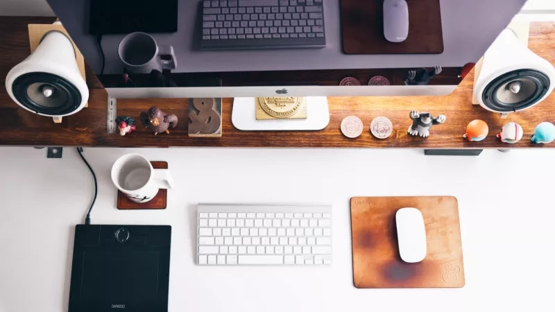 Computer workstation with keyboard, mouse, speakers, and figurines on a wooden desk.