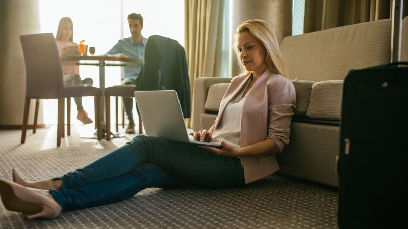 woman sitting on hotel floor with laptop and family at table