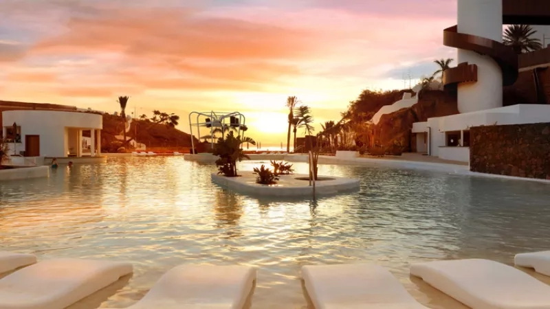 Outdoor pool with lounge chairs and a view of the sunset at sunset, surrounded by tropical plants.