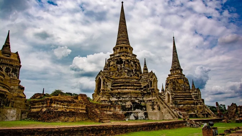Thailand, with an ancient temple, lush green lawn, and a cloudy sky in the background.