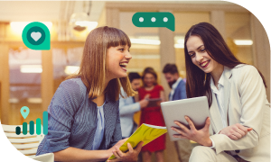 Two businesswomen discussing with a tablet in a meeting with others in a room with lights.