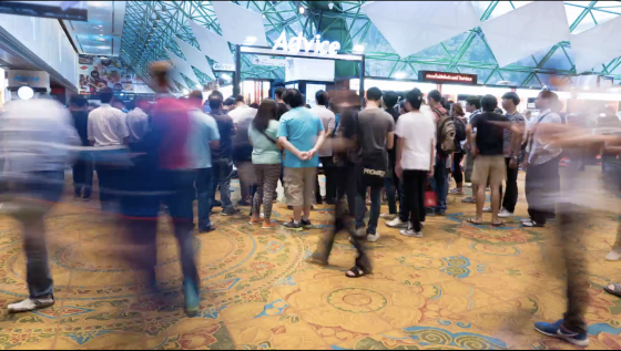 A crowd of people waiting in line in front of a counter inside an airport.