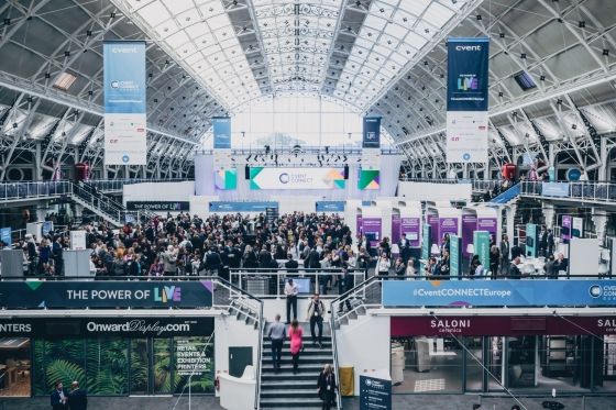 An image of a convention center showing the interior with banners and a crowd of people.