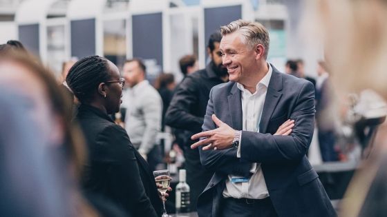 Man in business suit talking to woman with wine glass at an event.