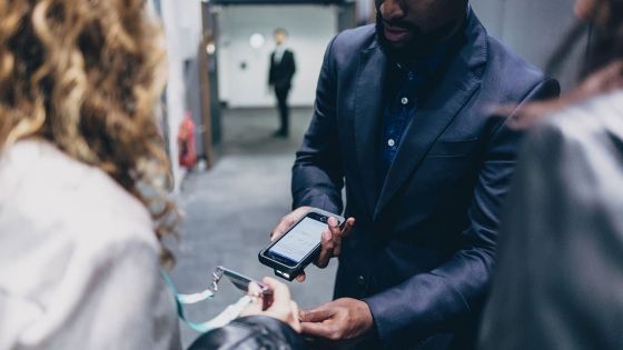 A man and a woman exchanging a badge with a smartphone in a corporate office.