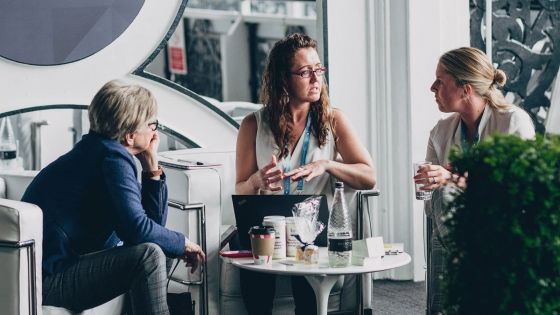Three women are sitting around a small table with food and drinks on it.