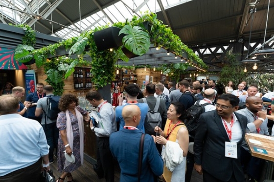 People gathered at a party in an indoor area with potted plants, a glass ceiling, and a wooden floor.