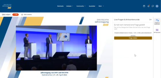 Screenshot of a website with three men standing on a stage in front of a large screen.