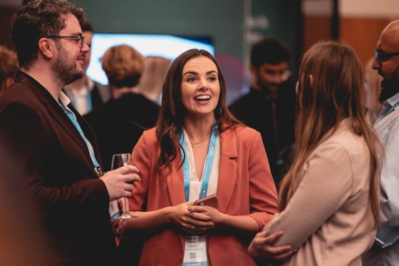Three smiling people networking at an event, with other people in the background.
