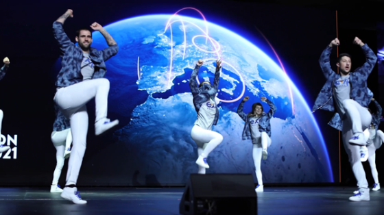 A group of people are dancing on stage with an image of the earth on the screen.