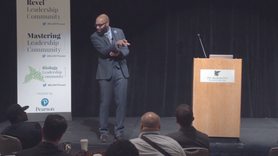 A man is standing on stage in front of a podium and a banner with the word "Pearson".