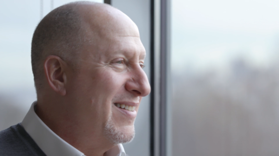 A bald man with a smile on his face and looking out of the window in the office.