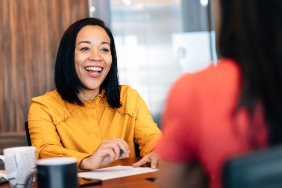A woman smiles while discussing something with another woman who is out of focus.