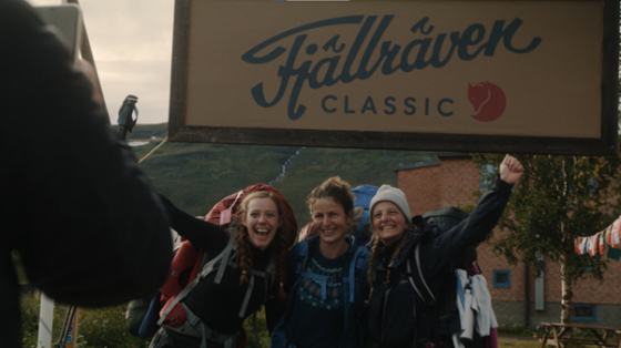Three hikers stand under the sign of Hallraven Classic with a building in the background.