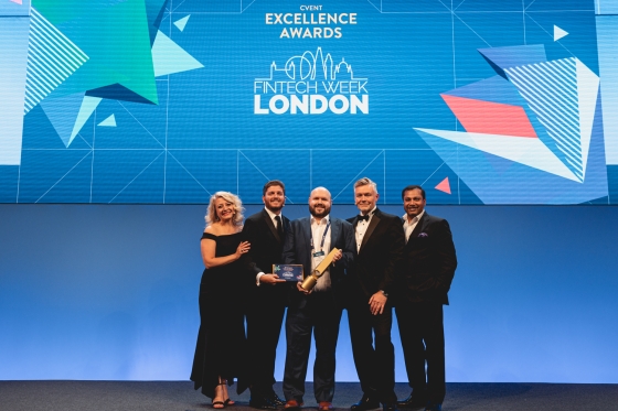 Four men and a woman pose with a trophy in front of a large screen.