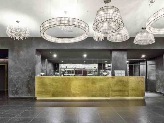 Modern reception desk with a gold finish and unique chandeliers hanging from the ceiling at MAXX by Vienna House.
