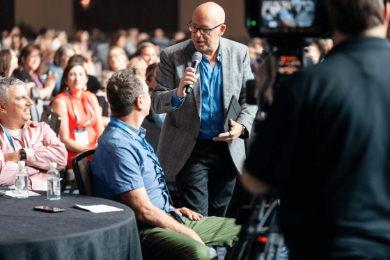 A person is holding a microphone in front of a camera in front of a crowd.