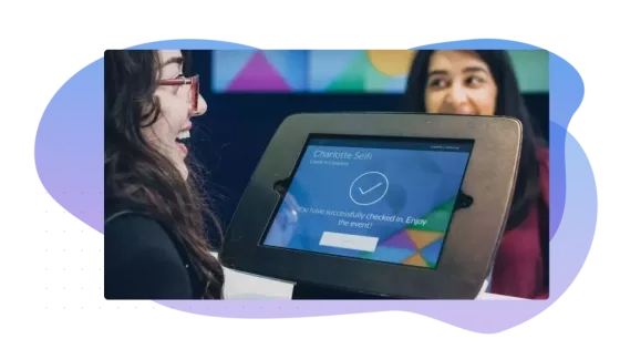 A woman smiling after checking in to an event using a kiosk with an interactive screen.