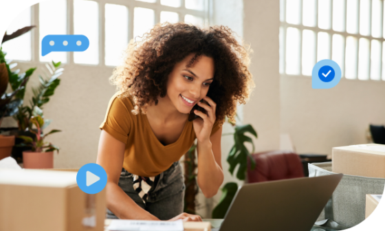 A woman is sitting at a desk talking on the phone and looking at a laptop.