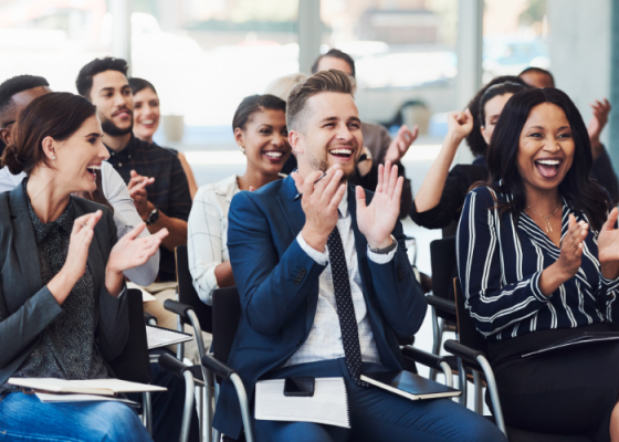 A group of people are seated in a row, clapping their hands and smiling at each other.