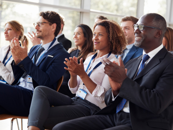 A group of people sitting in a conference room and clapping their hands in a happy mood.