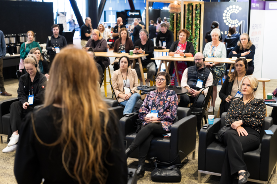A group of women at the conference, with one woman standing and the rest sitting.