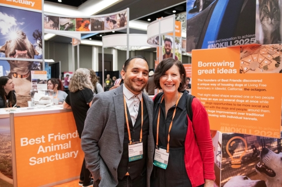 Marc Peralta and a woman stand in front of a Best Friends Animal Sanctuary booth at a conference.