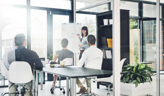 A group of people are sitting in a conference room while a woman is standing and presenting.