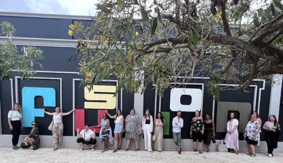 Group of people standing in front of FUSION building with tree and bright sky in background.