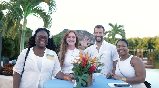 Four people smiling at the camera at a resort, with a tropical garden and pool in the background.