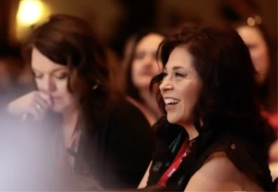 Woman smiling as she looks to her left with others in the background at the Women Supporting Women event.