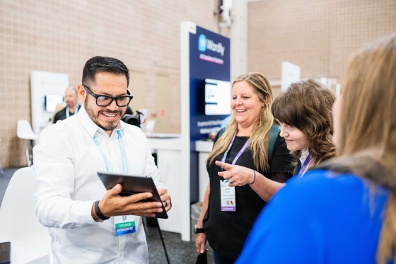 A group of three women and one man at a trade show talking about a tablet.
