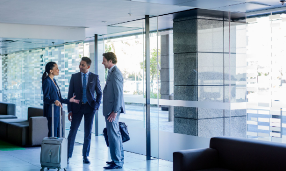 Three business people in suits talking to each other in a lobby with glass doors and windows.