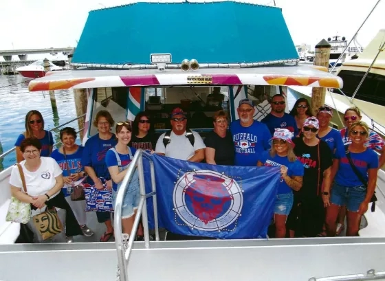 Group of people in blue shirts holding a blue flag on a boat in a marina.