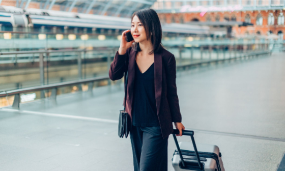 Woman walking with luggage and talking on a cellphone in an airport with a train in the background.