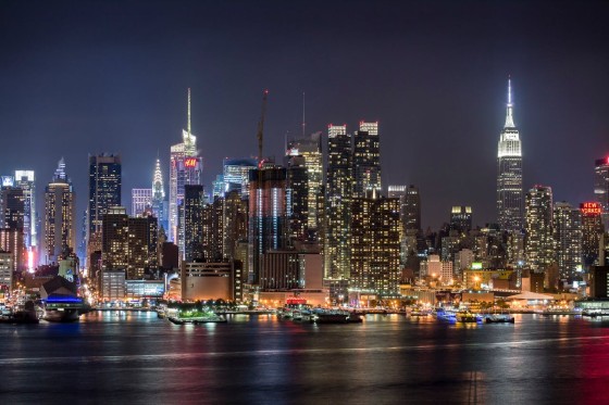 A night view of the city of New York with many buildings and a water body in front.