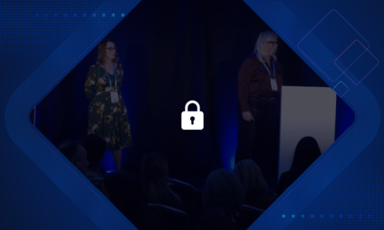 Two women standing on a stage in front of an audience with a padlock in the foreground.