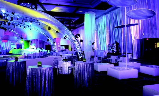 A dimly lit room with tables and chairs, and a stage in the distance.