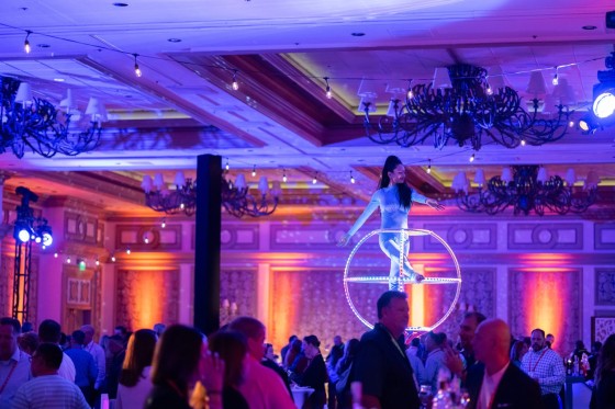A performer stands in a glowing ring above a large crowd in a banquet hall at Aria Resort & Casino.