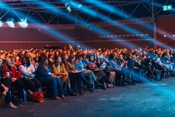 A group of people are sitting on chairs in a hall with stage lights.