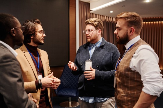 Four men are standing and talking to each other at an event inside a room.