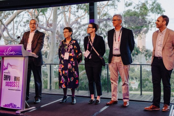 Five people stand on stage at Empowering Success, with trees and an outdoor deck behind them.