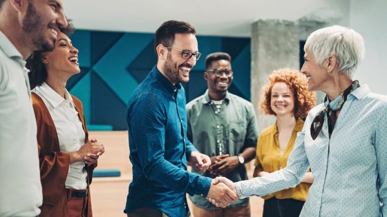 A group of diverse professionals are seen shaking hands and smiling in an office environment.