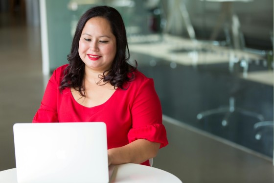 An adult woman with a red blouse is working on a laptop at an office.