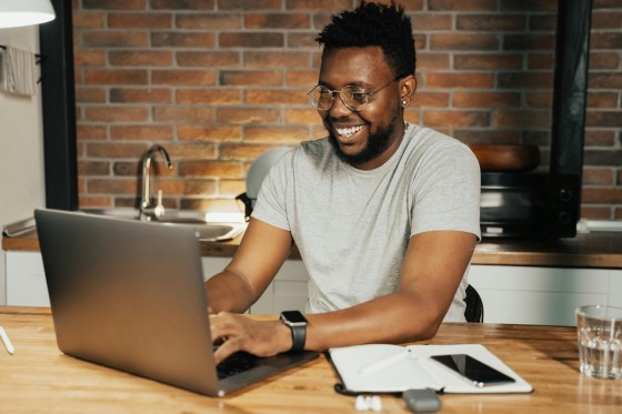 Man working at home on laptop with notebook, phone, and glass of water on wooden table.