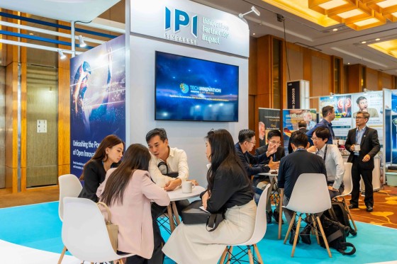 People are sitting at a table at an event, with a banner behind them that reads "Innovation Partner for Impact."