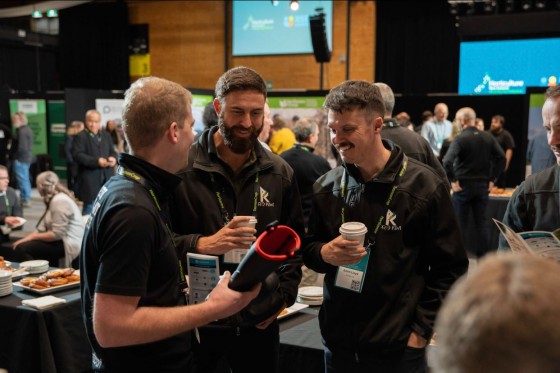 Three men wearing black jackets are chatting with each other at a conference event.